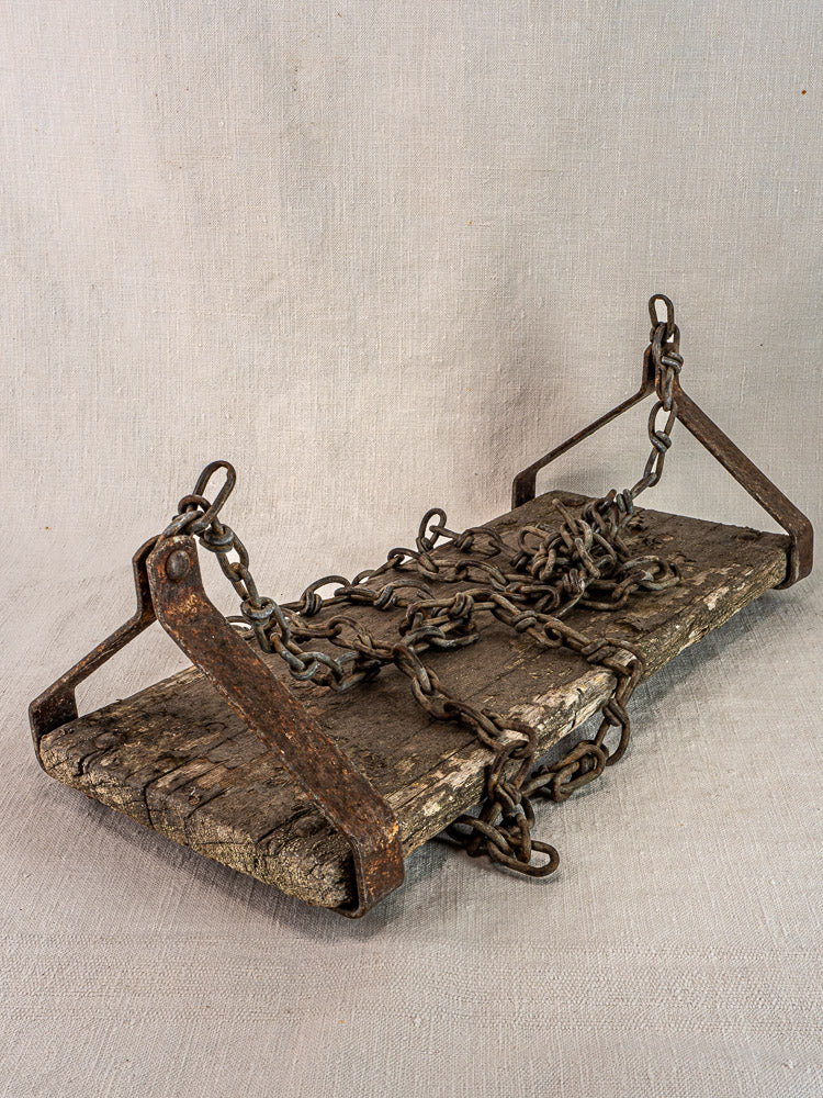 Antique French child’s wooden swing with iron brackets and rusty chains on neutral fabric background.