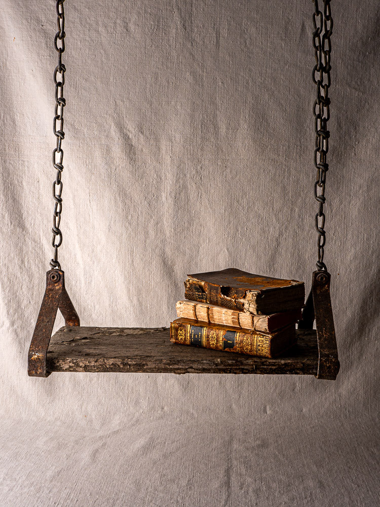 Antique French child’s swing in weathered wood and iron, with old books, neutral fabric backdrop.
