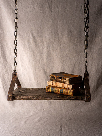 Antique French child’s swing in weathered wood and iron, with old books, neutral fabric backdrop.