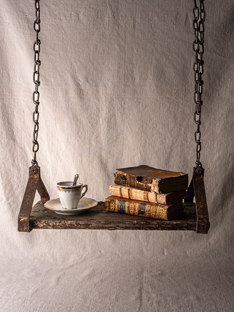 Antique French child’s swing in wood and iron with old books and teacup on neutral fabric.