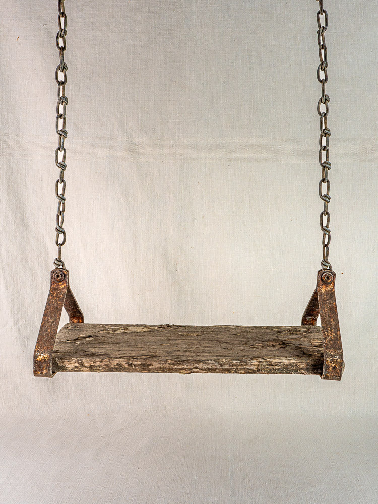 Antique French child’s swing, c. 1900, in wood and iron with aged metal chains, light fabric backdrop.