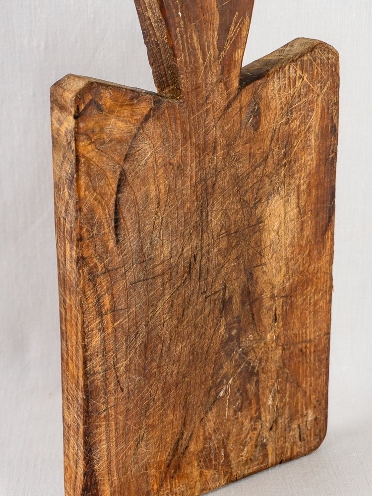 Antique French cutting board with faceted handle, worn 19th-century surface and visible scratches.