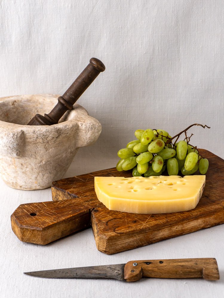 Antique French cutting board with faceted handle, topped with cheese, grapes, and mortar and pestle.