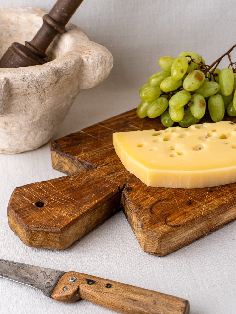 19th c. antique French cutting board with faceted handle, Swiss cheese, grapes, stone mortar and pestle.