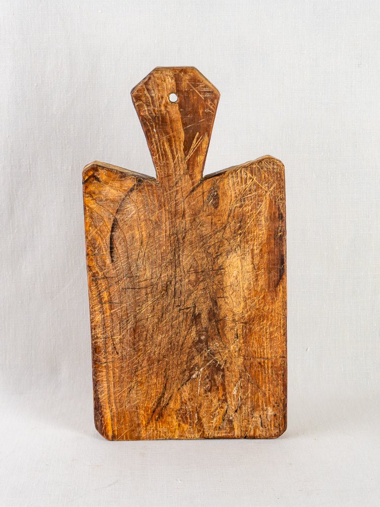 Antique French cutting board with faceted handle, knife marks, and worn surface on light background.
