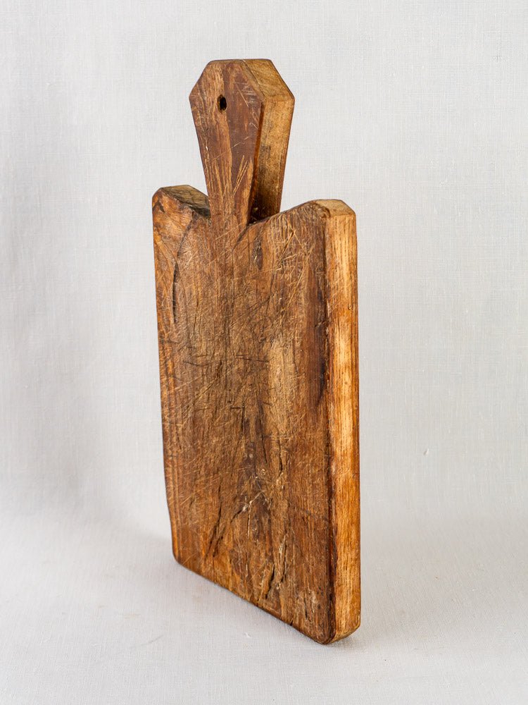 19th-century French antique fruitwood cutting board with faceted handle and rustic knife-marked surface.
