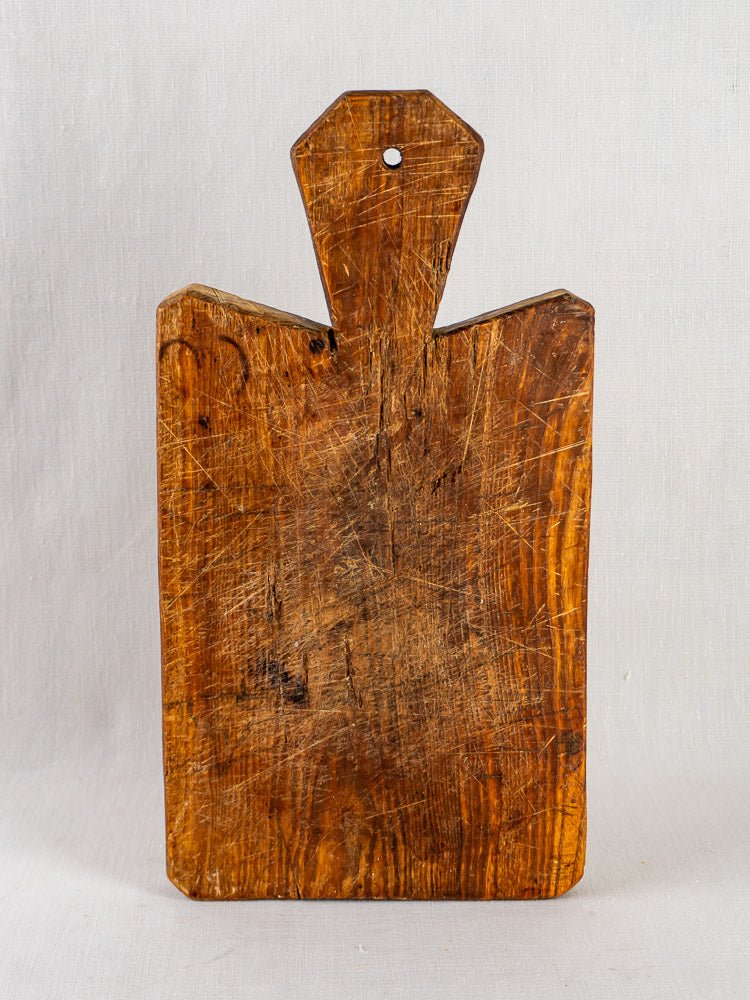 Antique French cutting board with faceted handle, 19th century, upright on light gray background.