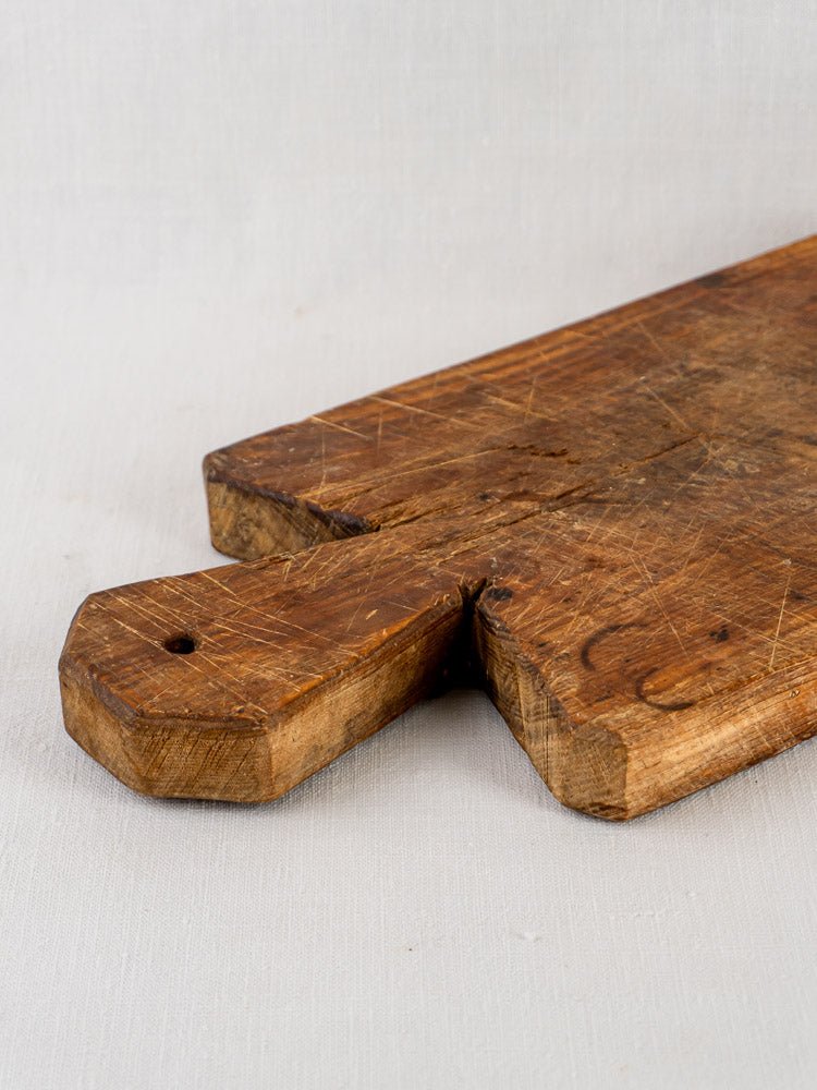 Antique French cutting board, 19th century, with faceted handle and knife-marked surface against light background.