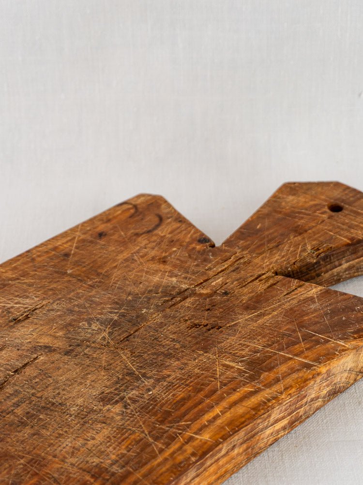 Antique French cutting board with faceted handle, worn surface and pierced handle on light background.