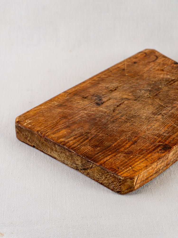 Antique French 19th-century rectangular cutting board with faceted handle and aged patina on light surface.