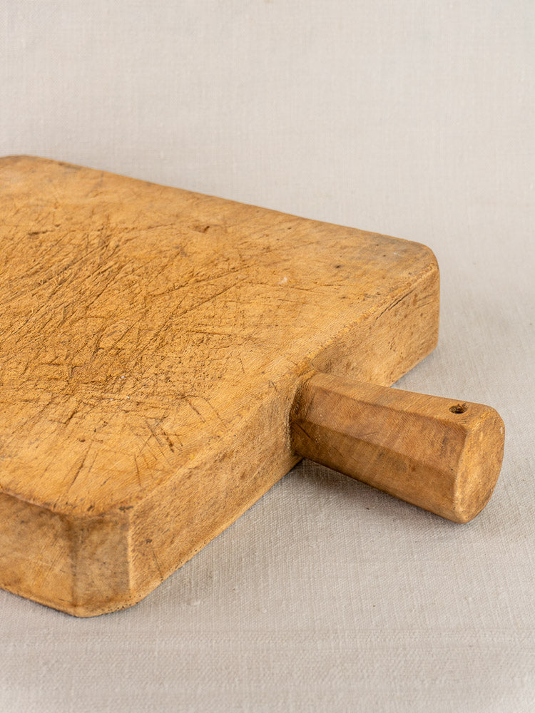 Antique French beech chopping board, square with a six-sided handle, surface marks, on a light textured background.