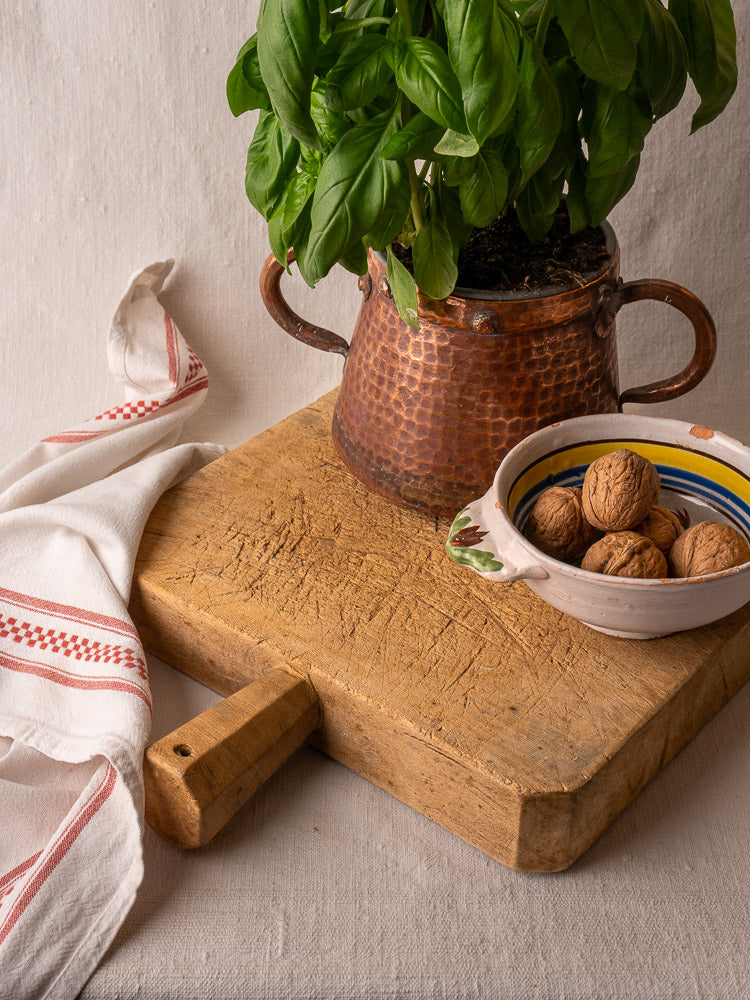 Antique French chopping board with square shape and six-sided handle, hand-carved, against a light background.