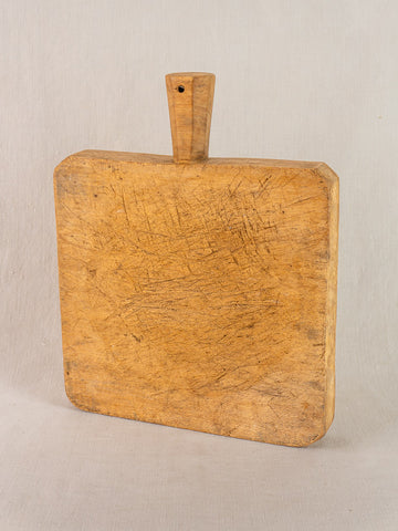 Antique French chopping board with square shape and six-sided handle, hand-carved, against a light background.