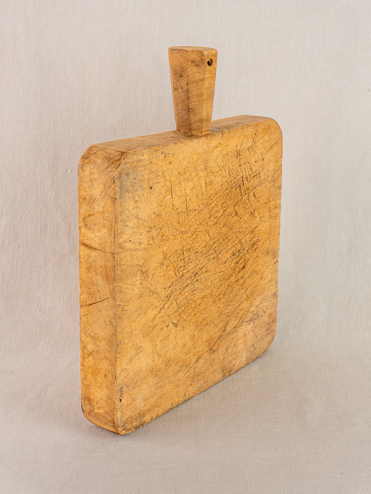 Antique French beech chopping board with six-sided handle and worn patina, shown upright against a neutral backdrop.