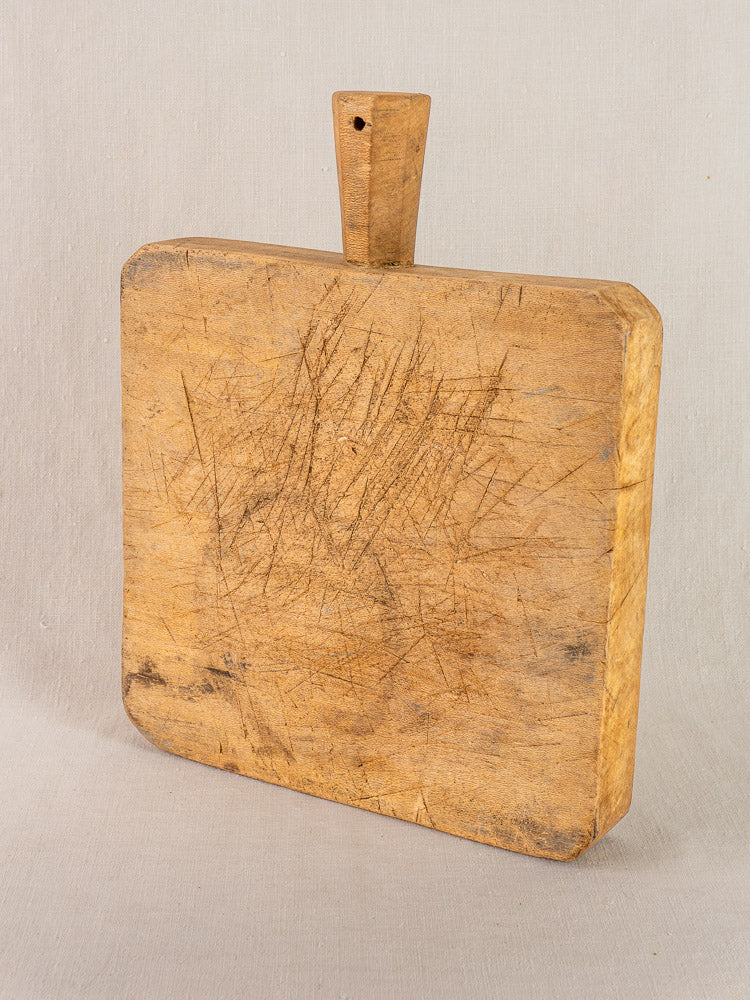 Antique French beech chopping board with six-sided handle, hand-carved and well-worn, on a light background.
