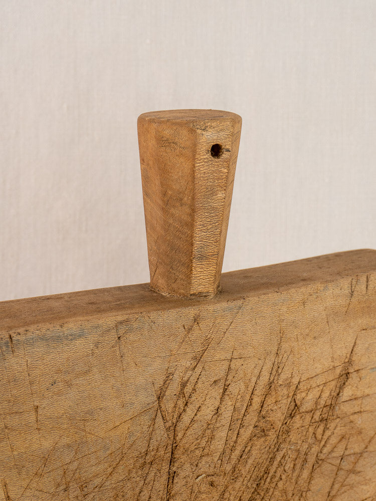 Antique French chopping board with six-sided handle, knife marks, and small top hole on a light background.