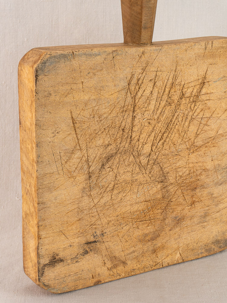 Antique French chopping board, square with six-sided handle, knife marks and scratches, upright on a light background.