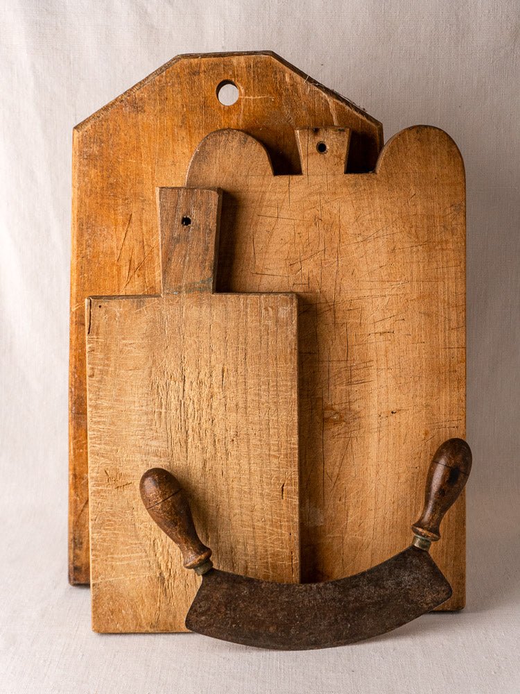 Set of three 19th-century French hardwood cutting boards with double-handled herb chopper, on neutral fabric.