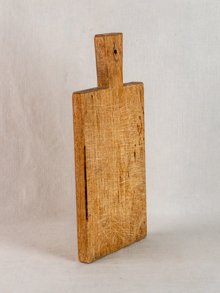 Antique French hardwood cutting board with rectangular shape and handle on a light surface.