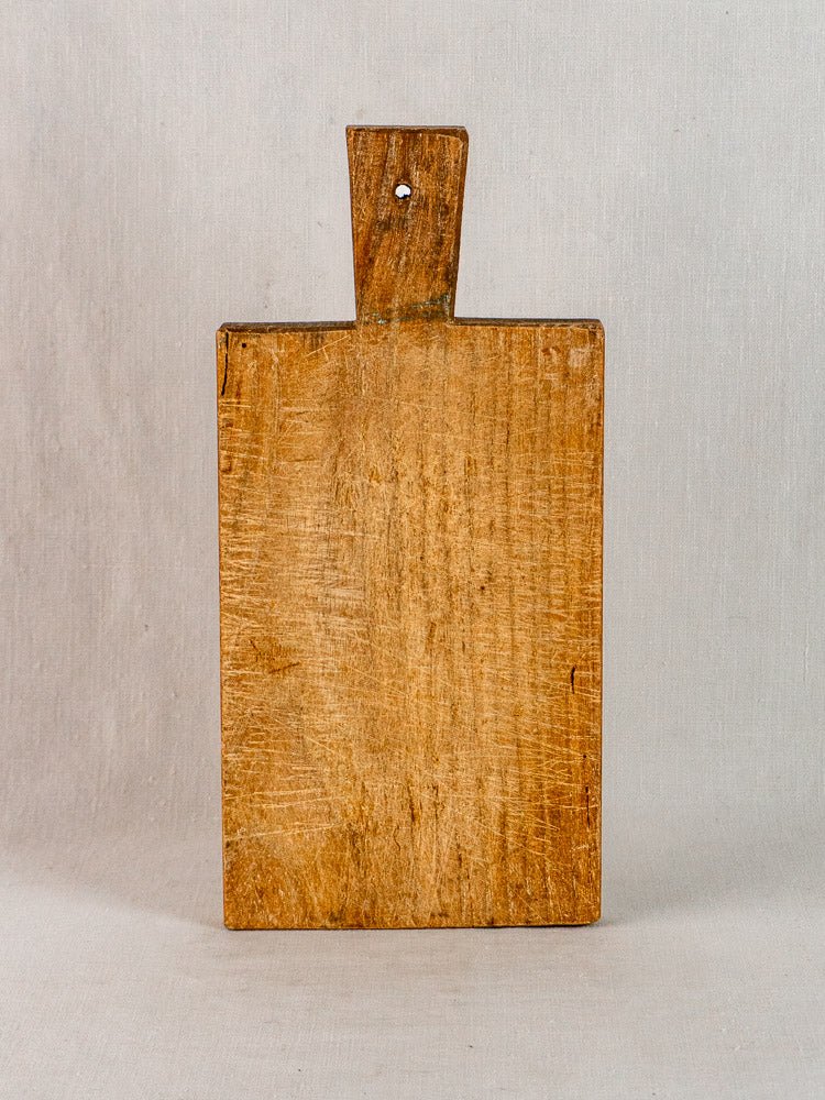 19th-century French antique hardwood cutting board, hand-cut, upright by its handle with hole, plain background.