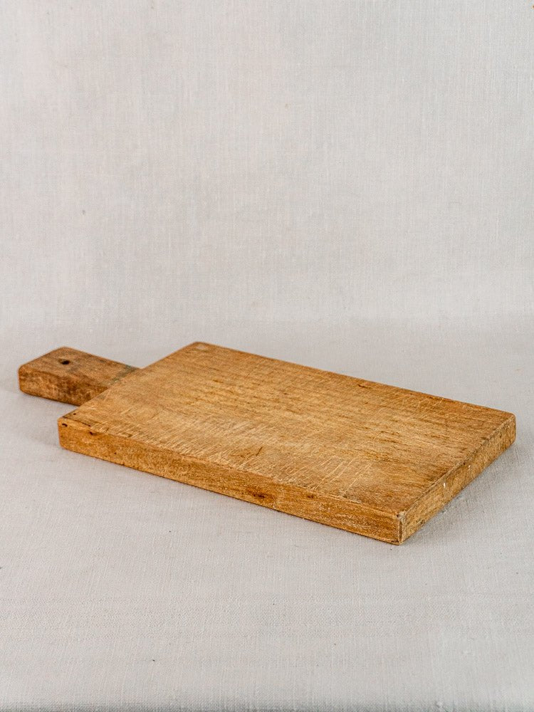 Antique French hardwood cutting board, 19th century, rectangular with short handle, on light fabric surface.