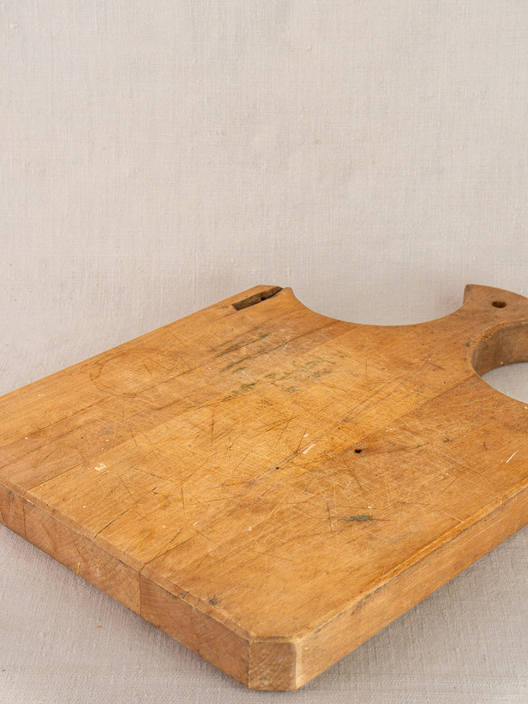 Antique French cutting board with fan handle and knife marks on a light gray textured surface.