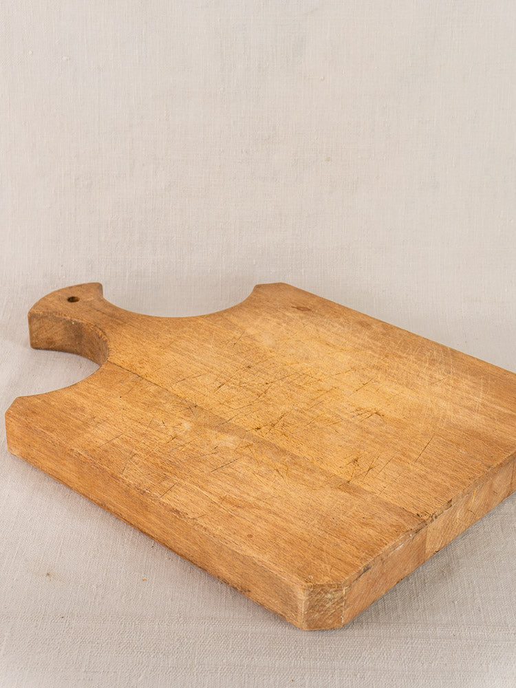 Antique French cutting board with fan-shaped handle and knife marks on light fabric surface. Late 19th century.