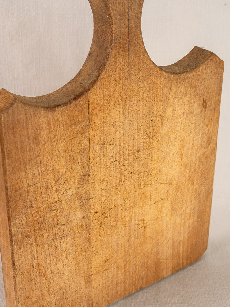 Antique French cutting board with fan-shaped handle, natural wood grain, and vintage scratch marks from frequent use.