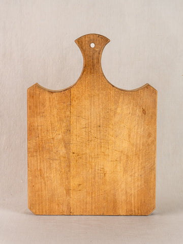 Antique French cutting board with fan-shaped handle from the 19th century, upright on a light surface, plain background.