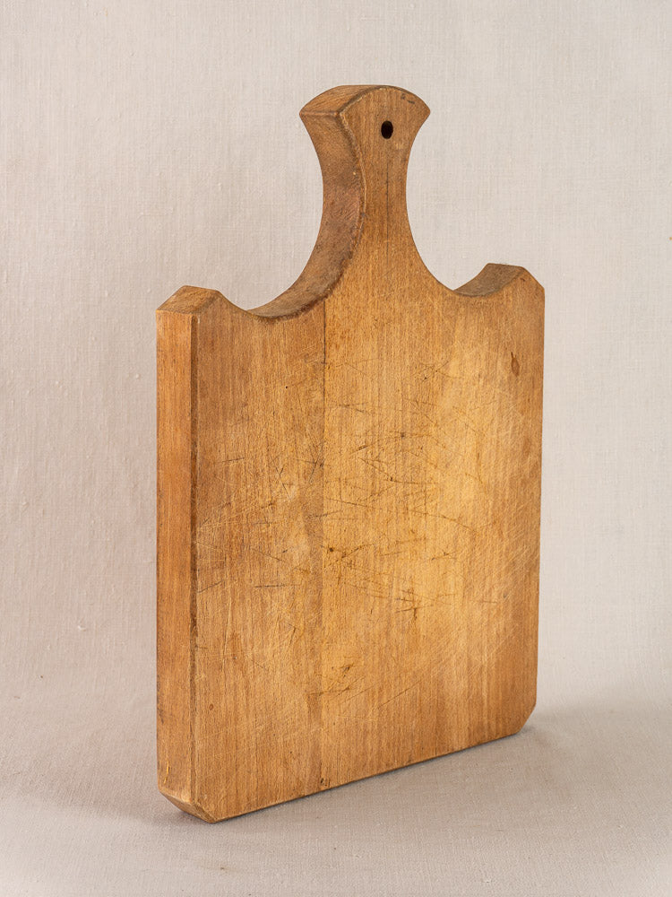 Late 19th century French beech wood cutting board with fan handle, hanging hole, and worn knife-scarred surface.