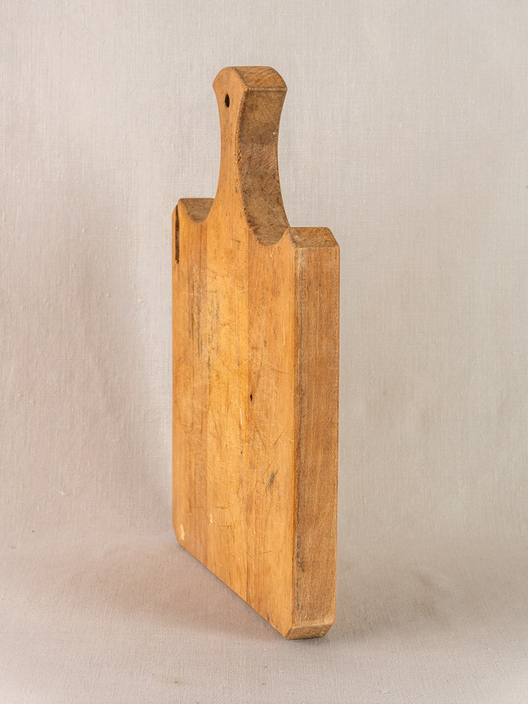 Antique French cutting board with fan handle, late 19th century, upright showing patina and knife marks on neutral background.