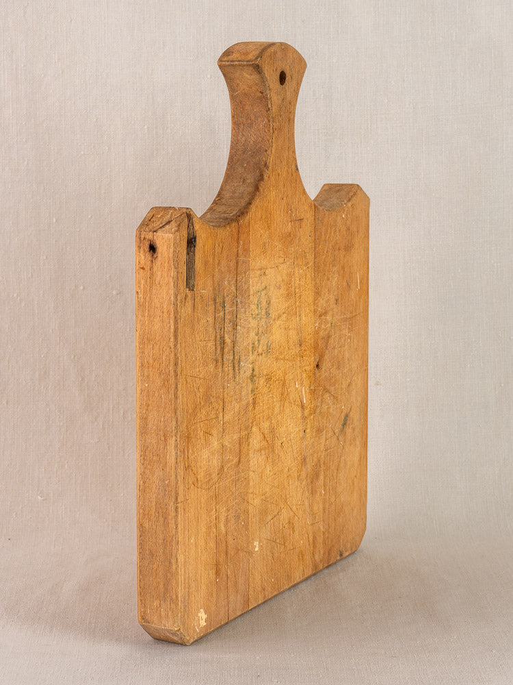 Late 19th-century French antique cutting board with fan-shaped handle, upright, displaying charming aged patina and wear.