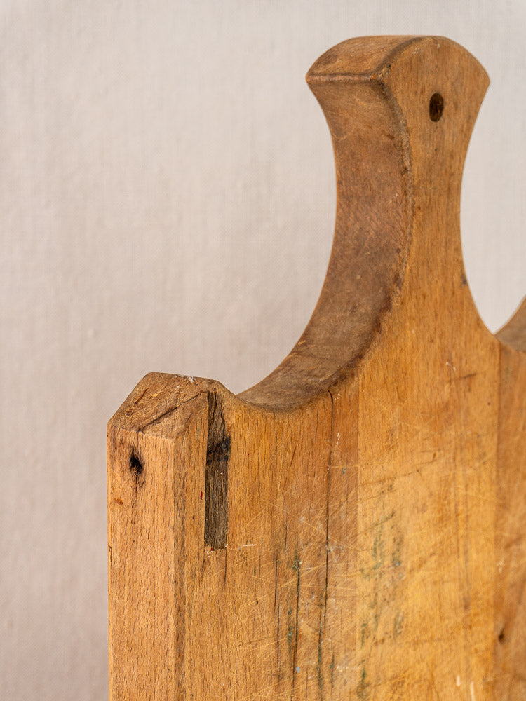 Antique French cutting board, late 19th century, fan handle, visible grain, scratches, side notch on light fabric background.