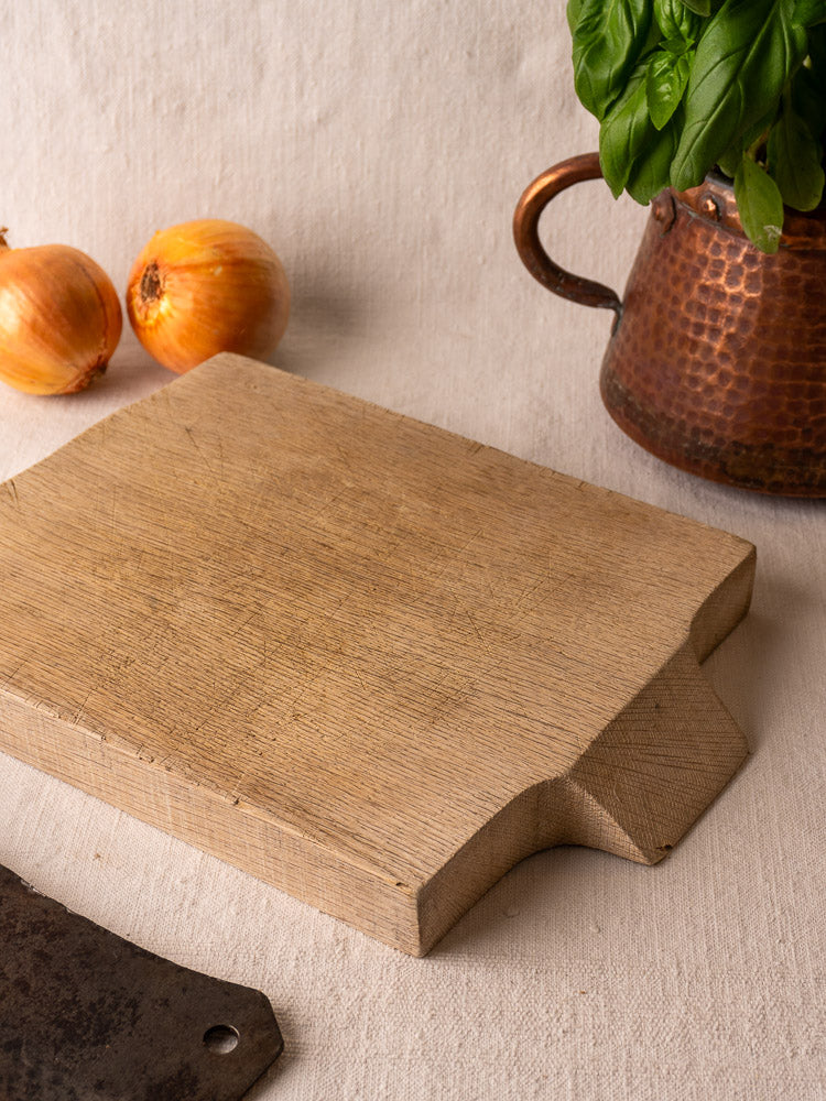 Antique French solid oak cutting board, circa 1900, on beige cloth with onions and vintage copper basil pot.