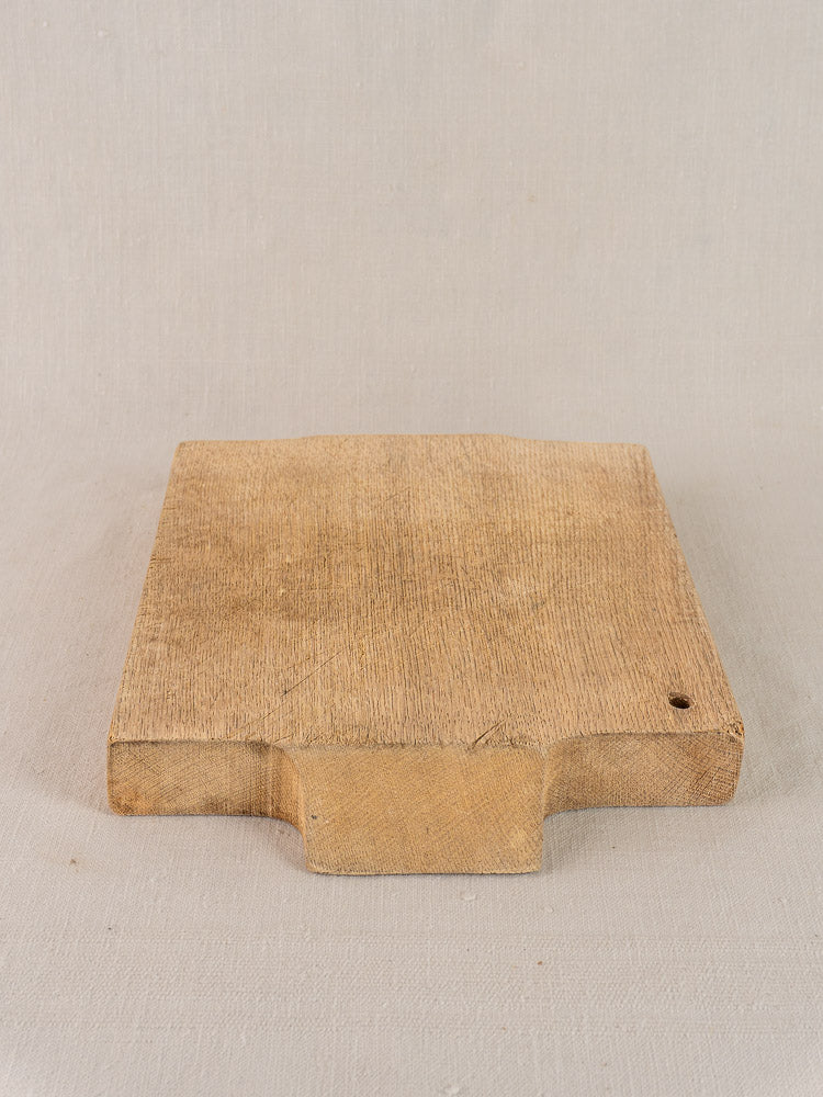 Antique French solid oak cutting board, rectangular with handle and hanging hole, on a light fabric surface.