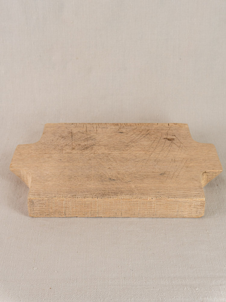 Antique French solid oak cutting board, rectangular with dual side notches, set on a light fabric background.