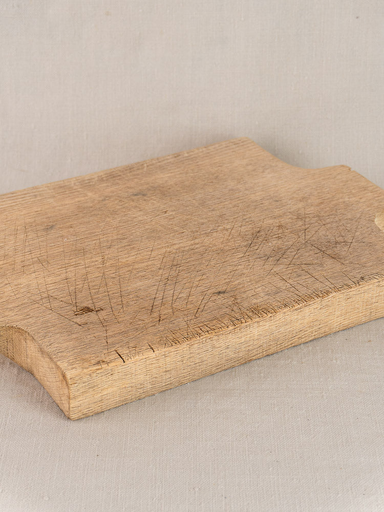 Antique French solid oak cutting board circa 1900 with knife marks, rustic edges on light beige fabric background.