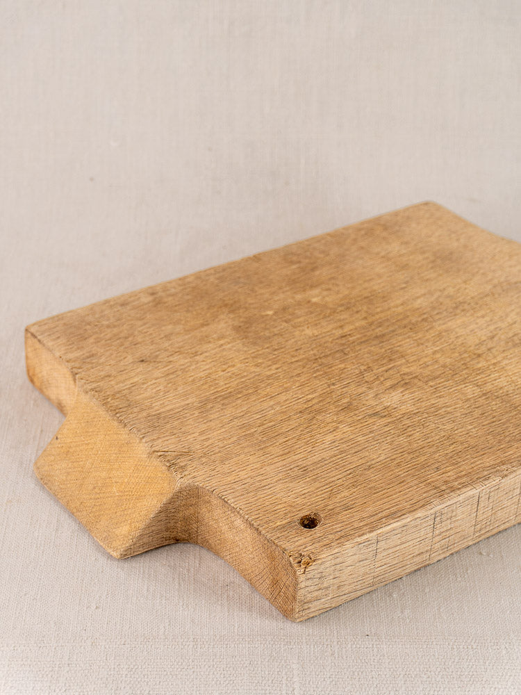 Antique French solid oak cutting board, rectangular with notched handle and hole, on light beige fabric surface.