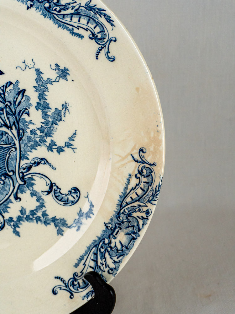 Vintage French ceramic plate with blue floral motifs on cream, rim worn and lightly discolored.