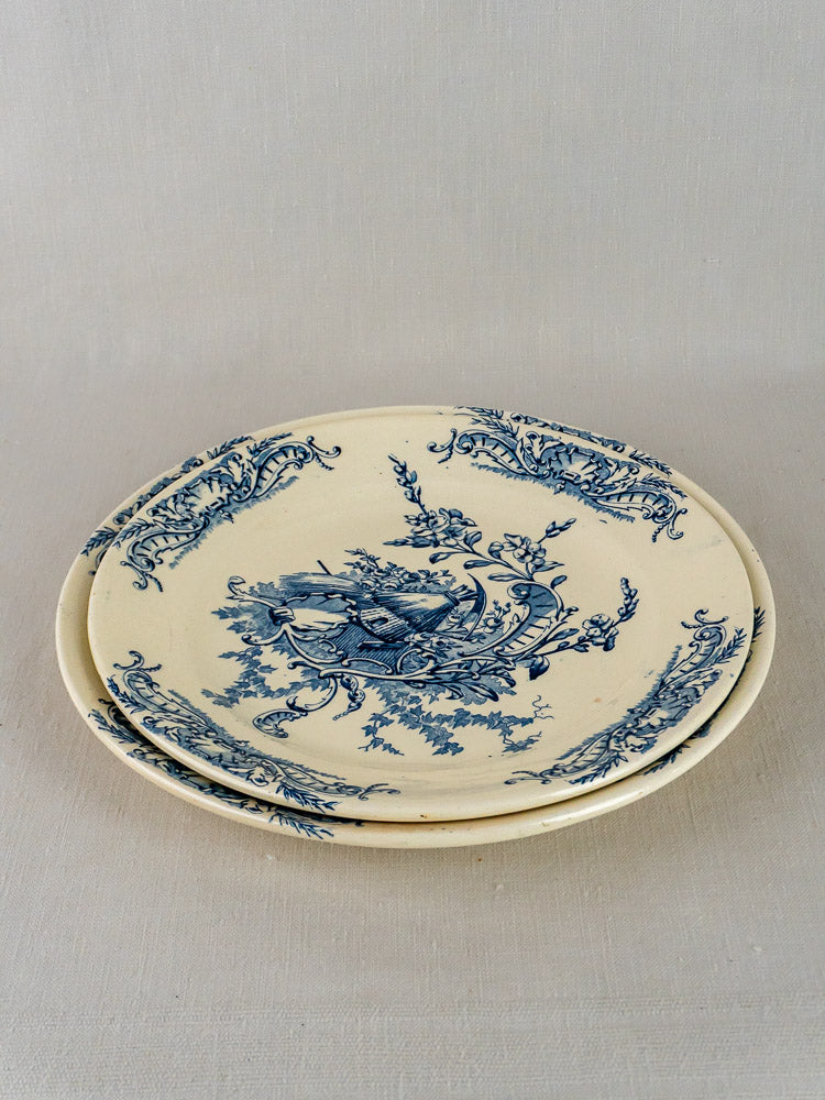 Pair of cream ceramic Louis XV Clairefontaine serving platters with blue floral Terre de Fer designs stacked on beige surface.