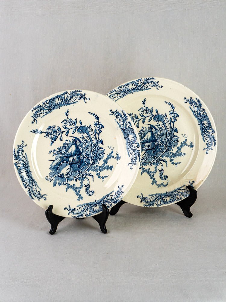 Pair of Clairefontaine Louis XV French Terre de Fer ceramic platters with blue floral cottage designs on black stands.