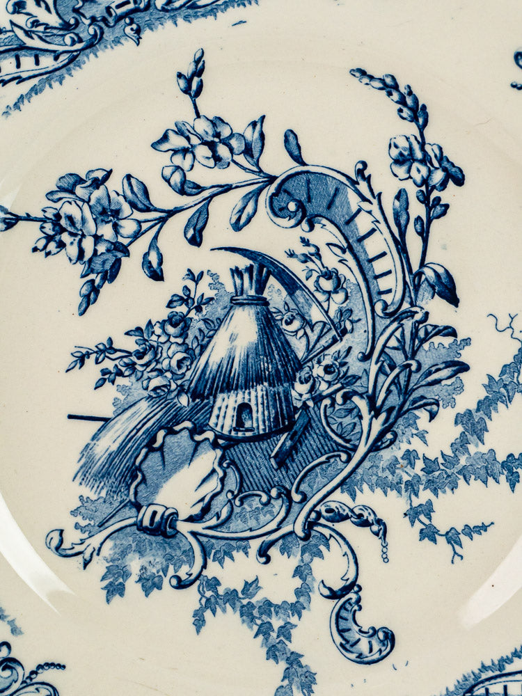 White ceramic terre de fer plates with blue floral scrollwork and central thatched hut scene.