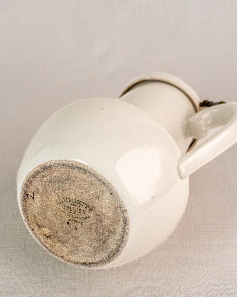 Early 20th-century Frugier Aluminite Limoges porcelain coffee pot showing stamped base on light fabric.