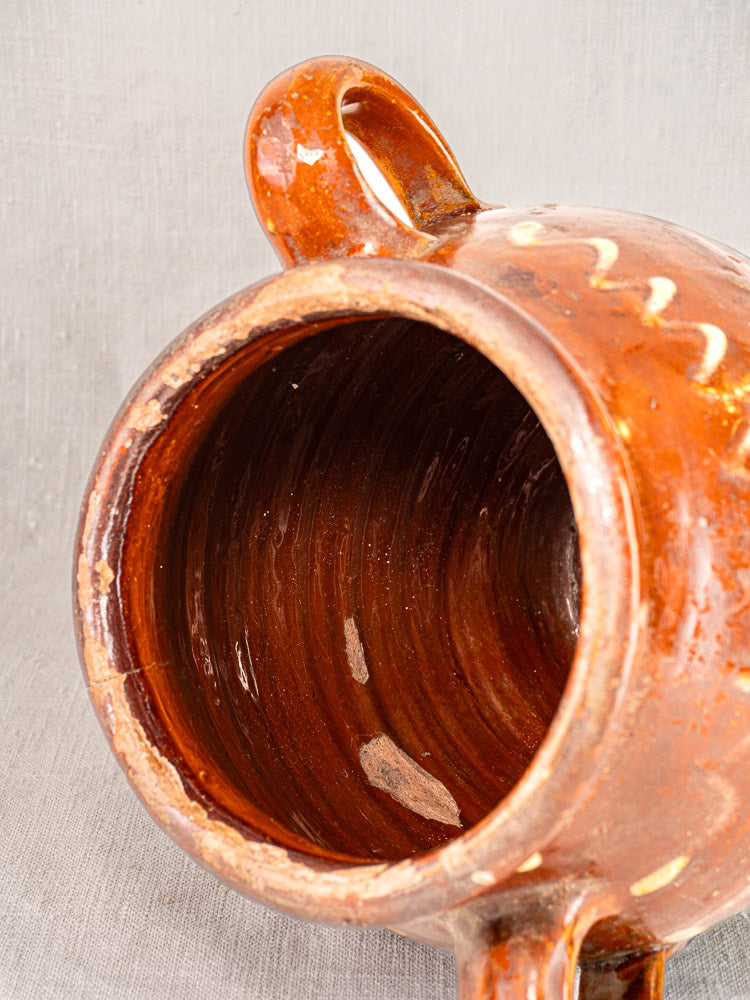 Antique French confit pot, mid-19th century, brown glaze, yellow slipwork, twin handles; gray fabric backdrop.