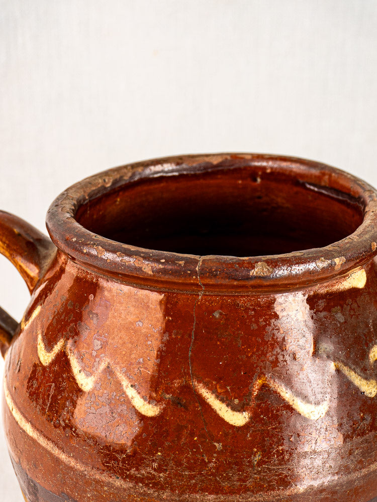 Antique French confit pot, mid-19th century, brown glaze, yellow slipwork, wavy lines, visible wear and textured surface.