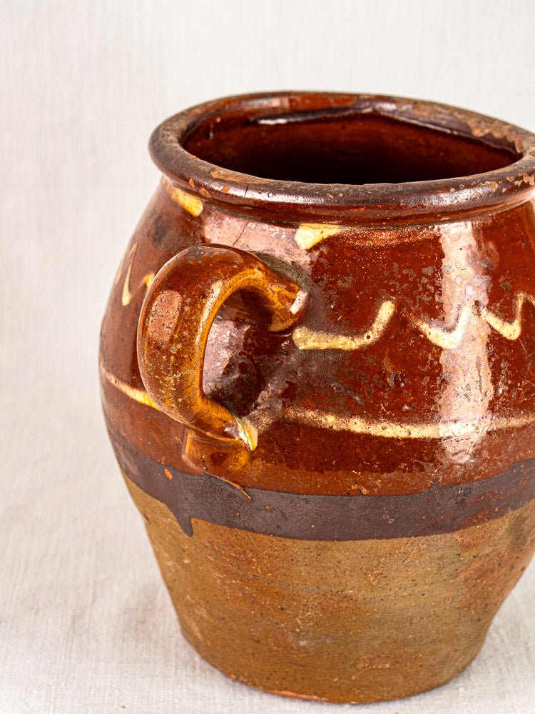Mid-19th-century French confit pot with single side handle, glossy brown glaze, yellow slipwork, unglazed textured base.