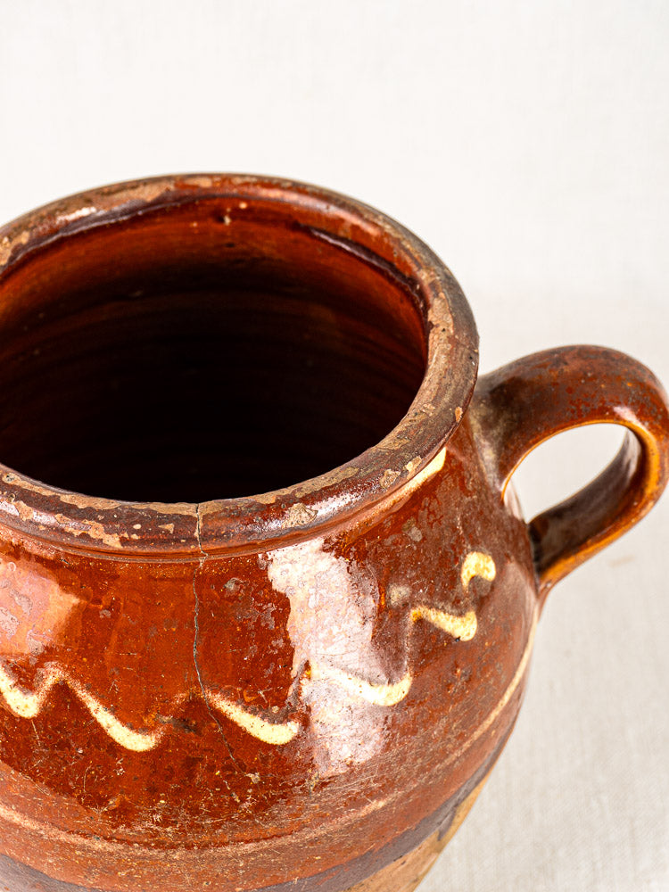 Antique French confit pot with brown glaze, yellow slipwork, handle, wide opening, and visible rim crack.
