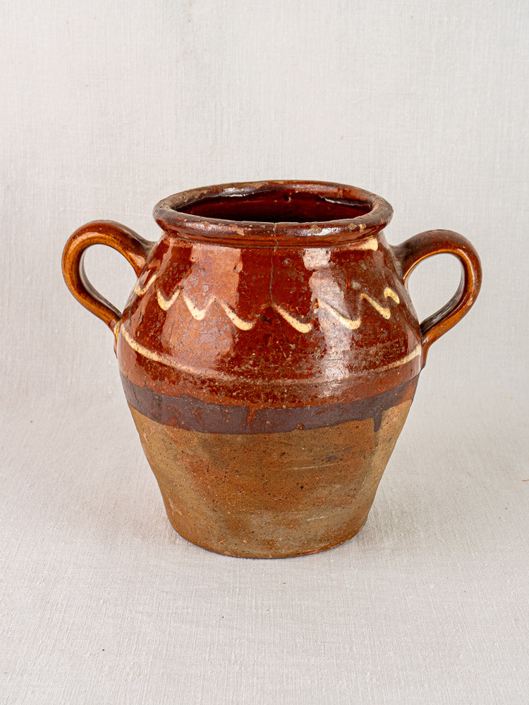 Antique French confit pot, mid-19th century, brown glaze with yellow slipwork, on plain surface.