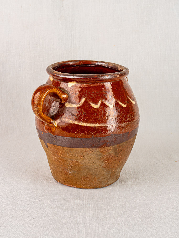 Large mid-19th century French confit pot in rustic brown ceramic with yellow slipwork, single handle, on a light background.