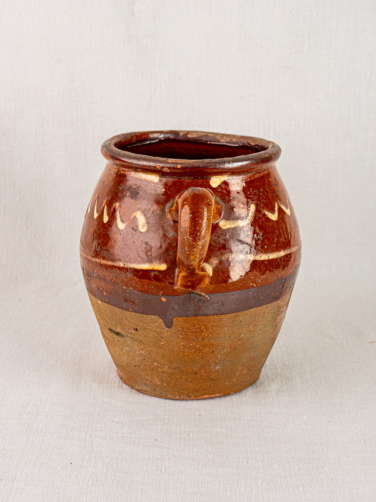 Antique French confit pot with rustic brown glaze, wavy cream slip, rounded body, and single handle.